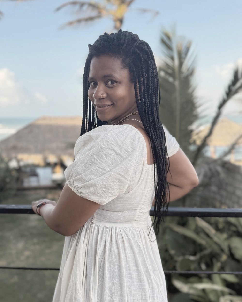 Tima Camara in a white dress, smiling over her shoulder by the sea